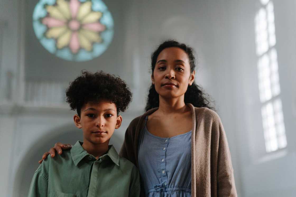 A woman stands with a young boy inside a church with stained glass. A woman stands with a young boy inside a church with stained glass.