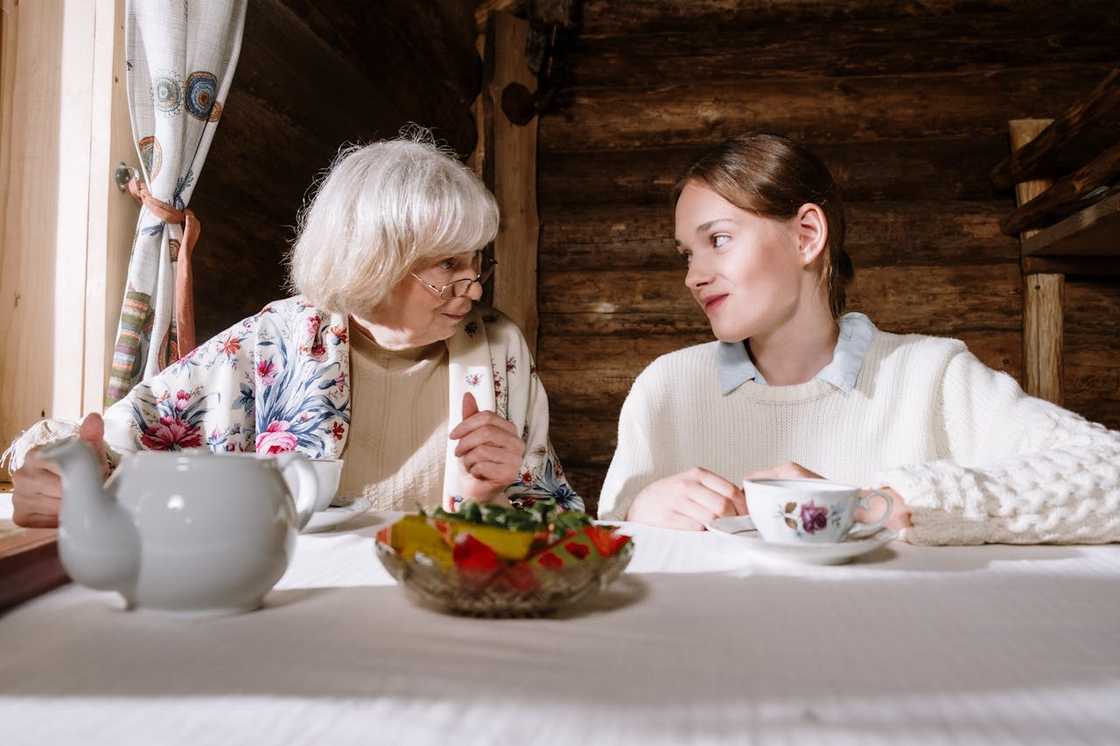 An old and a young woman sharing tea at table.