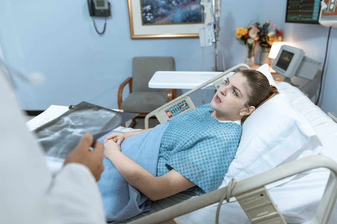 A woman lying in a hospital bed as a doctor reviews her X-ray. A woman lying in a hospital bed as a doctor reviews her X-ray.
