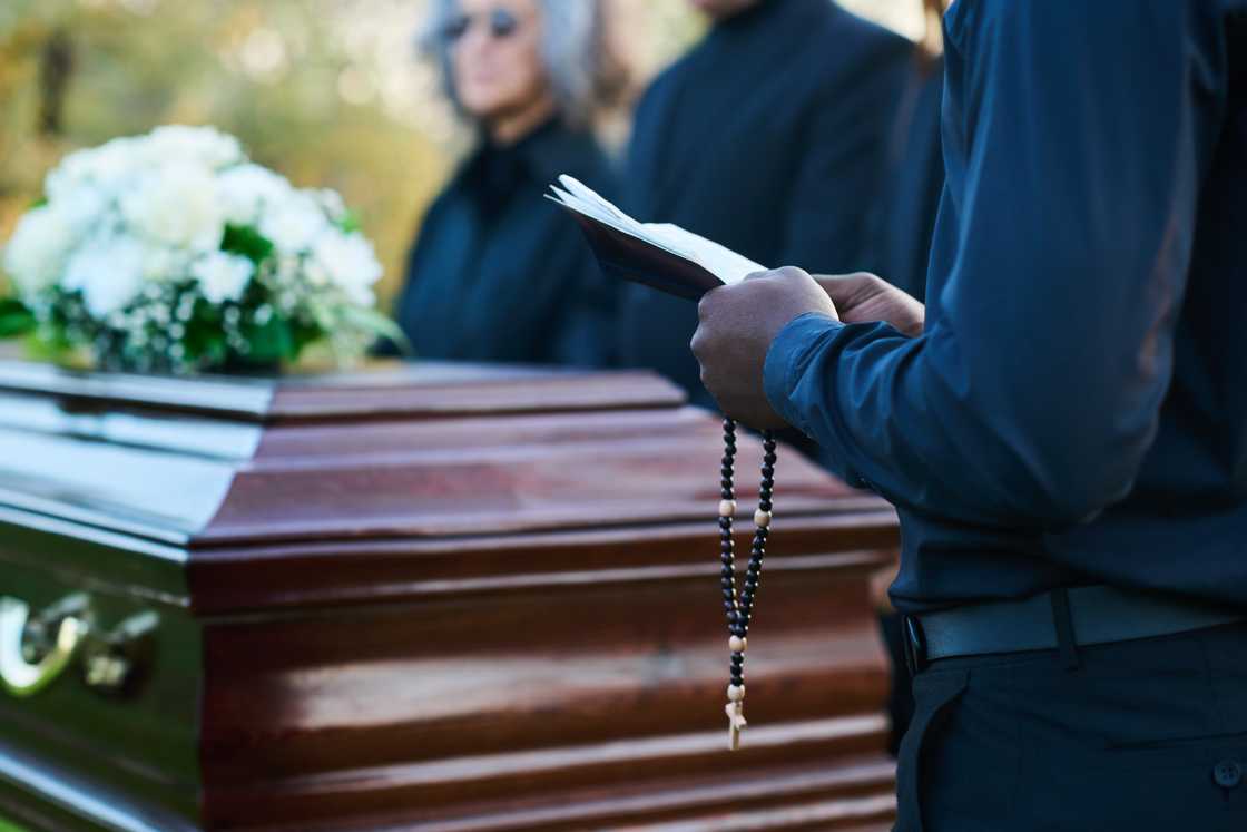 A coffin surrounded by mourners in black.