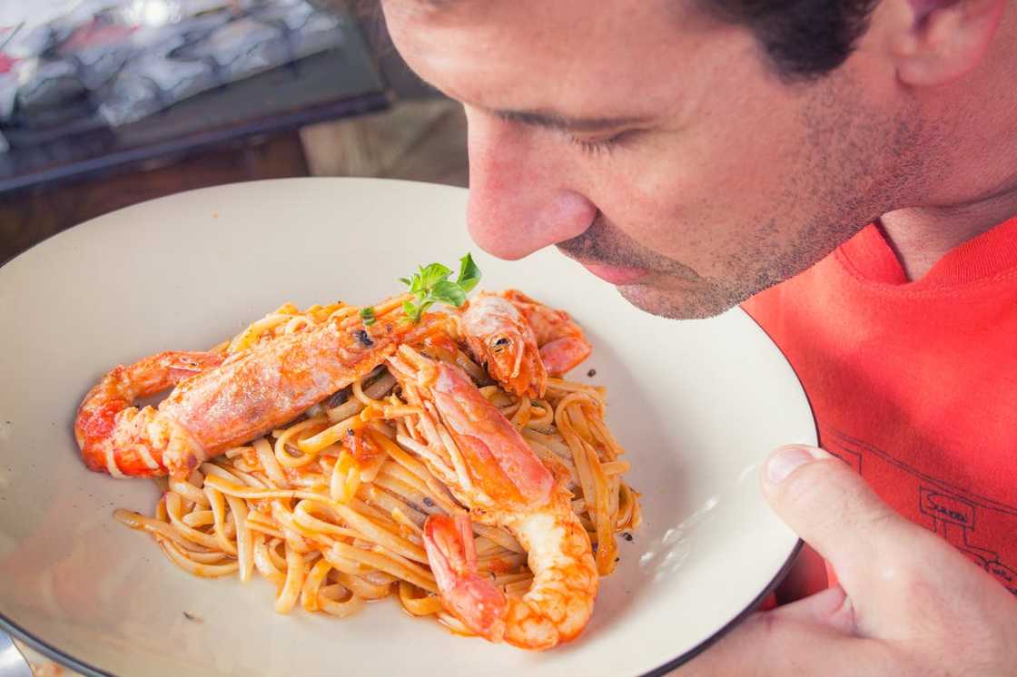A man smelling a plate of shrimp pasta before eating.
