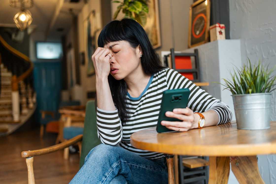 A stressed woman while using a smartphone in a coffee shop A stressed woman while using a smartphone in a coffee shop