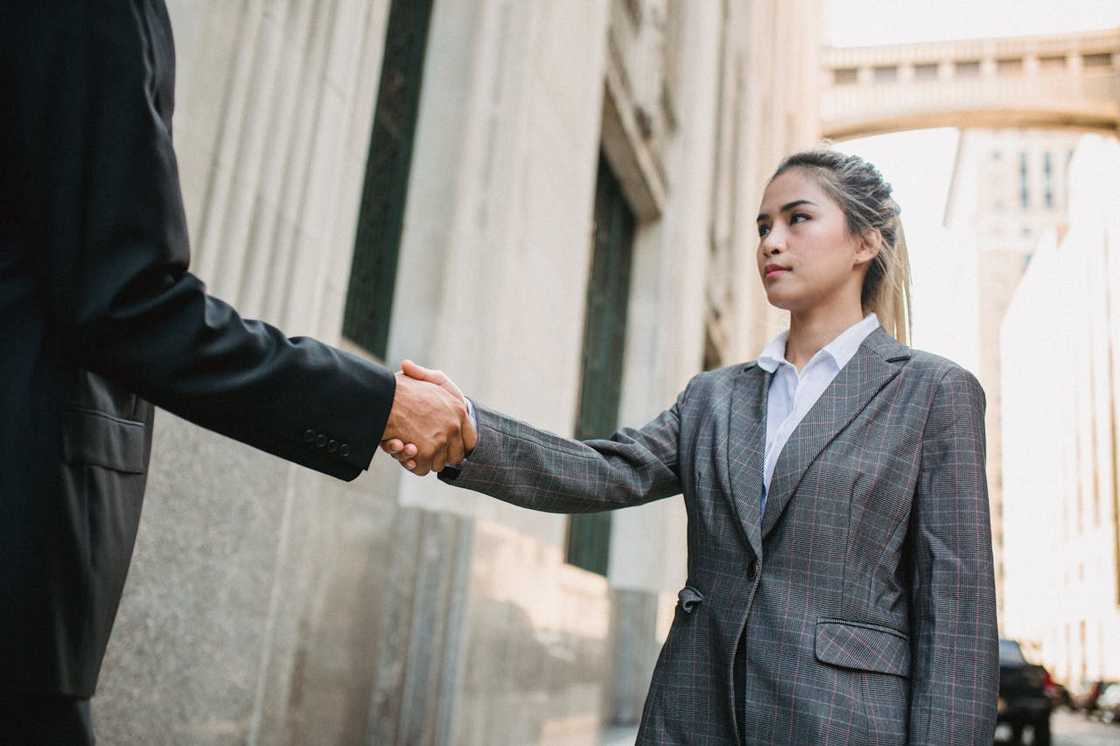 A woman in a business suit shakes hands with a man outside an office building. A woman in a business suit shakes hands with a man outside an office building.