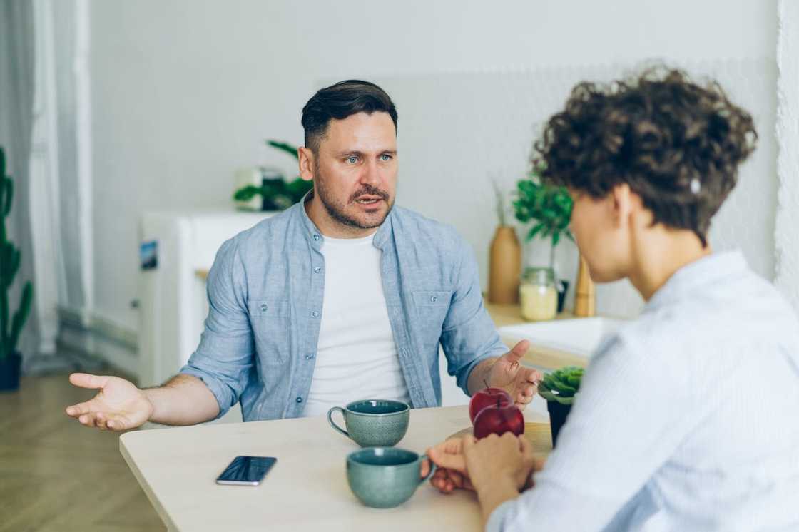A man gestures with open hands as he speaks to another person seated across the table.