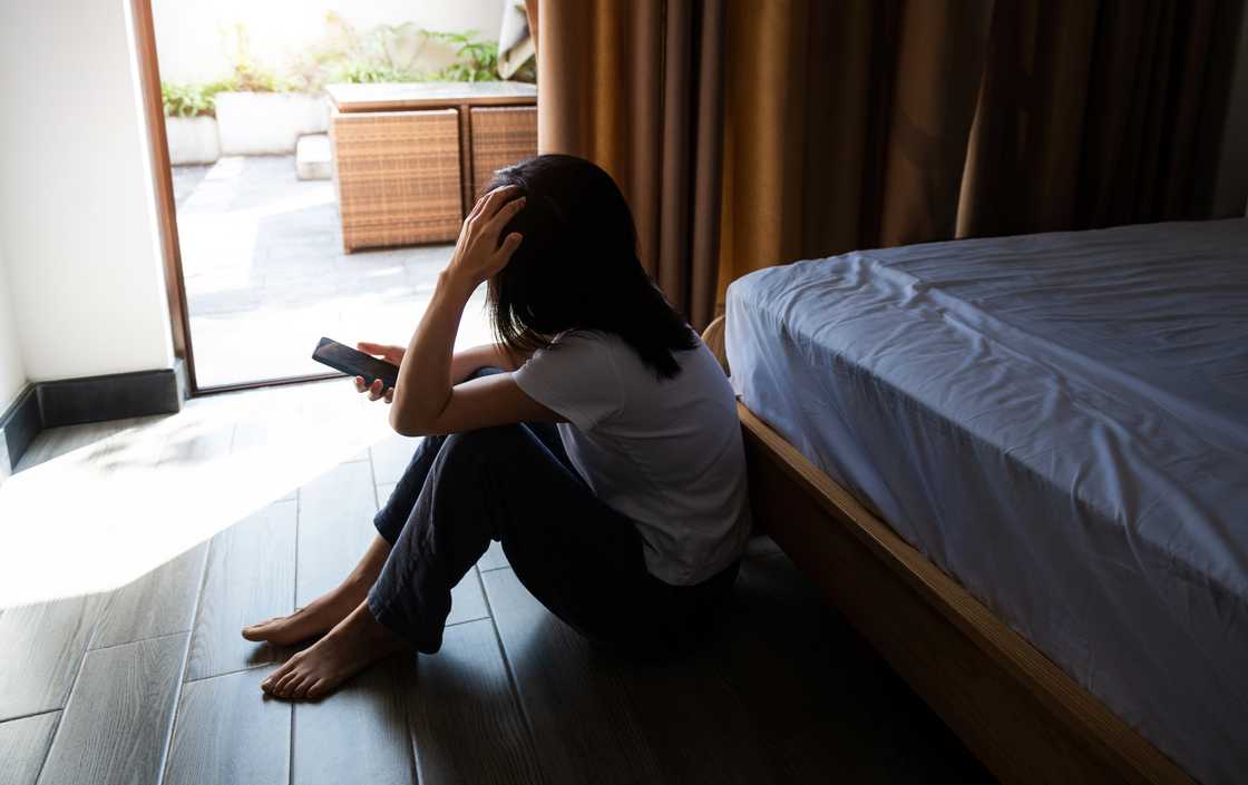 A lady sits on the bedroom floor while using her phone