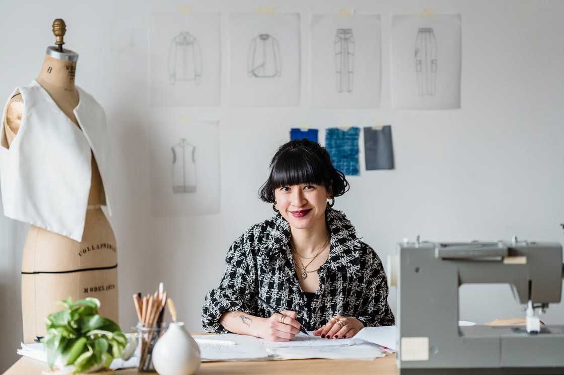 Fashion designer sketching at a worktable beside a dress form and sewing machine.
