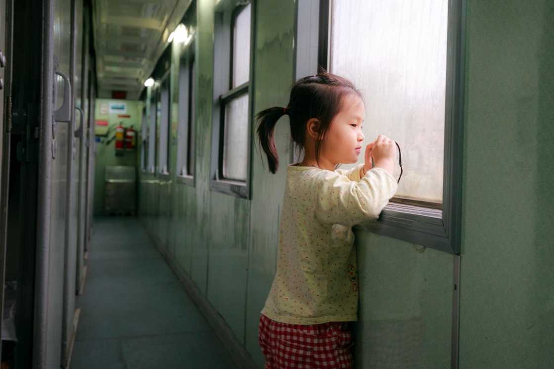 A young girl stares out a window in a hallway.