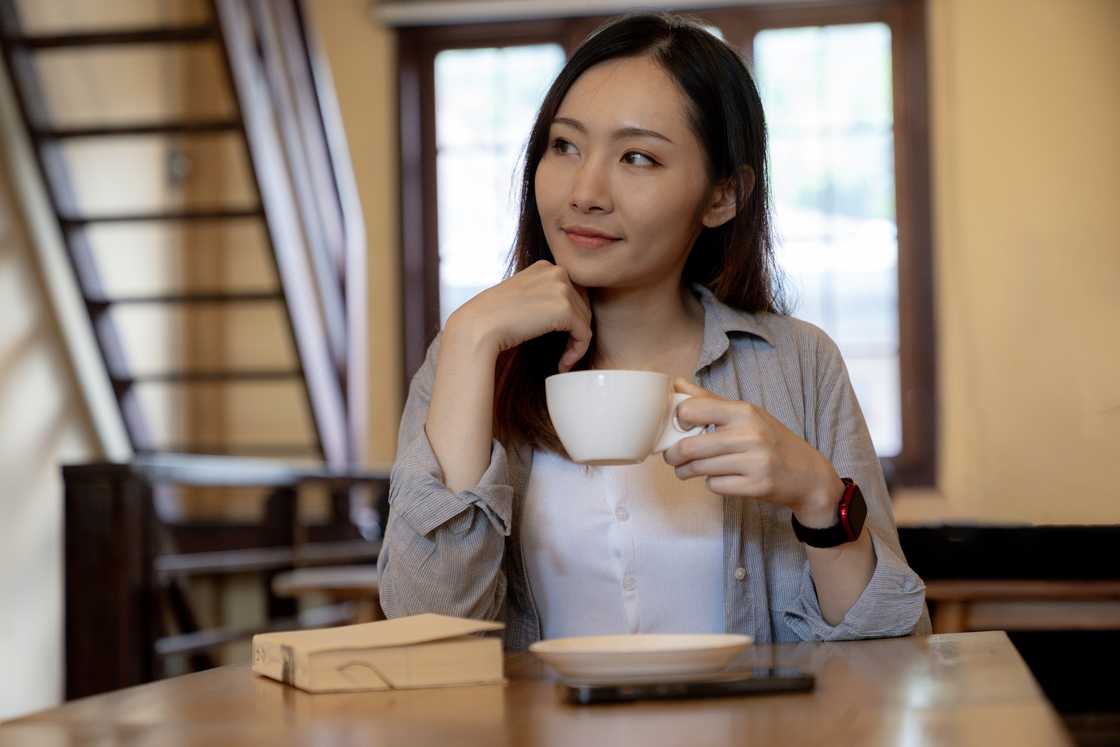 A happy woman reflecting on her life as she hold a cup of tea A happy woman reflecting on her life as she hold a cup of tea