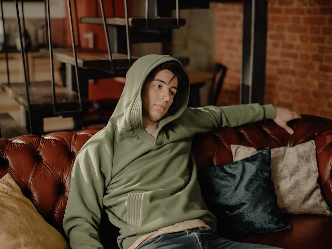 A young man relaxes on a leather couch, appearing drained as he stares off in contemplation. A young man relaxes on a leather couch, appearing drained as he stares off in contemplation.