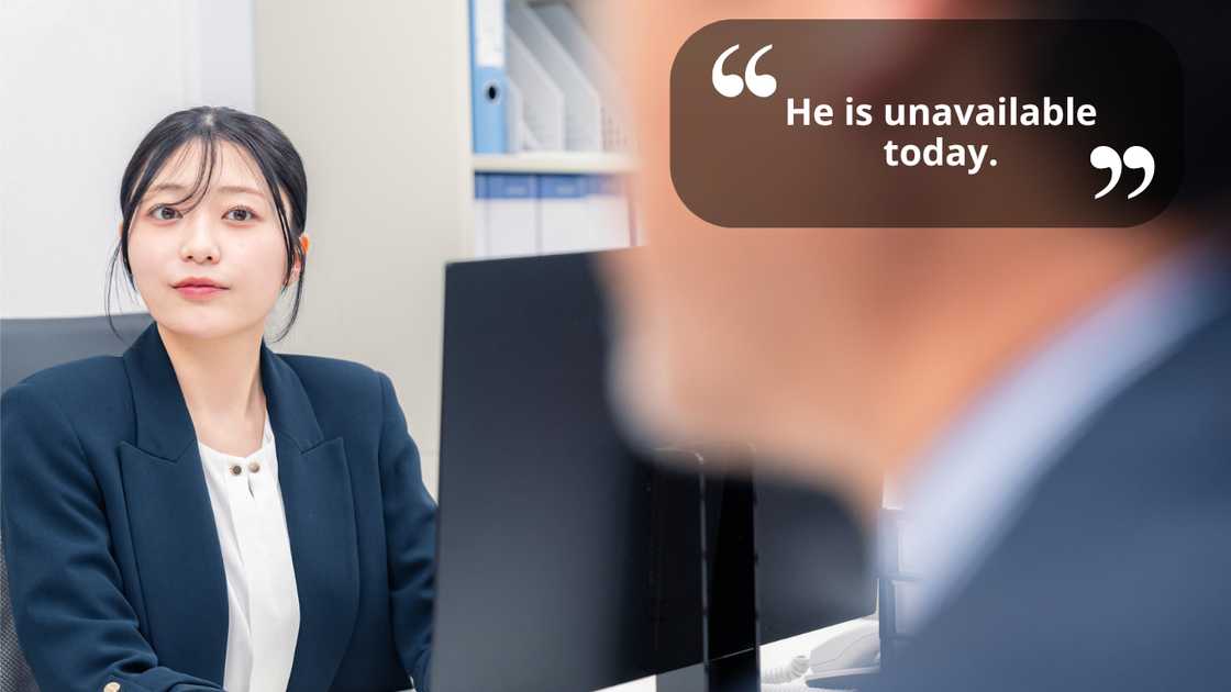 A young woman working at a desk while talking to a colleague A young woman working at a desk while talking to a colleague