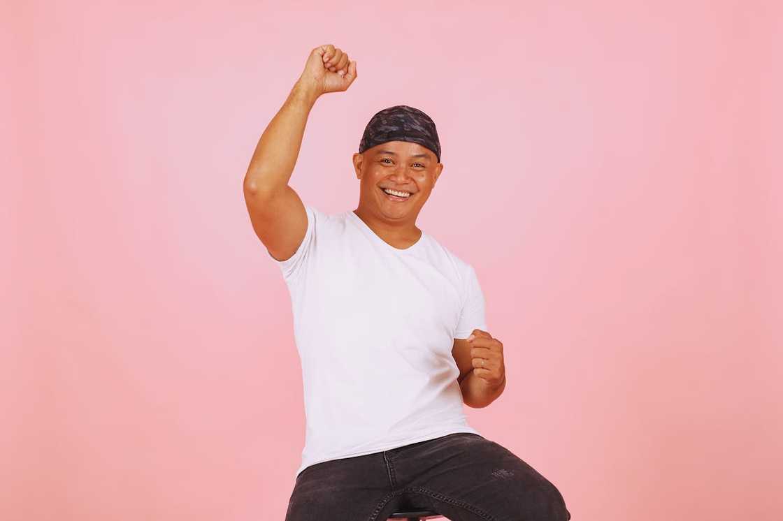 A smiling person raises a fist in celebration against a pink background.