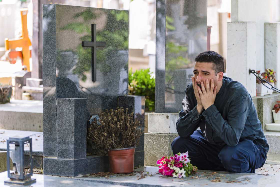 A sad and emotionally broken man is sitting at the cemetery. A sad and emotionally broken man is sitting at the cemetery.