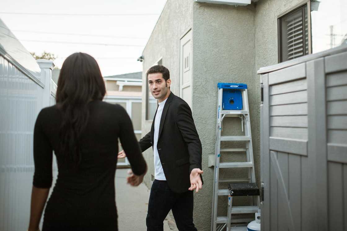 A man gestures toward a woman during a tense exchange in a narrow outdoor walkway. A man gestures toward a woman during a tense exchange in a narrow outdoor walkway.