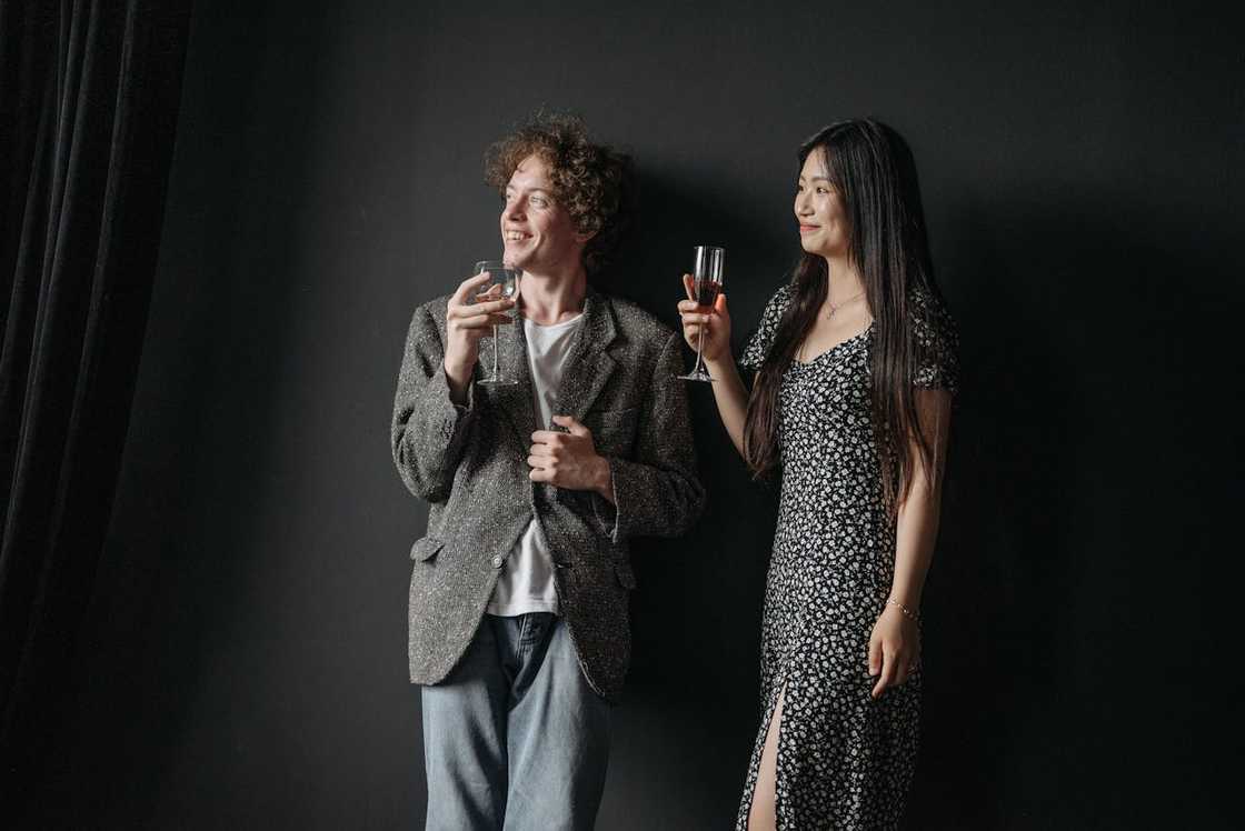 Two people stand while holding wine glasses. Two people stand while holding wine glasses.