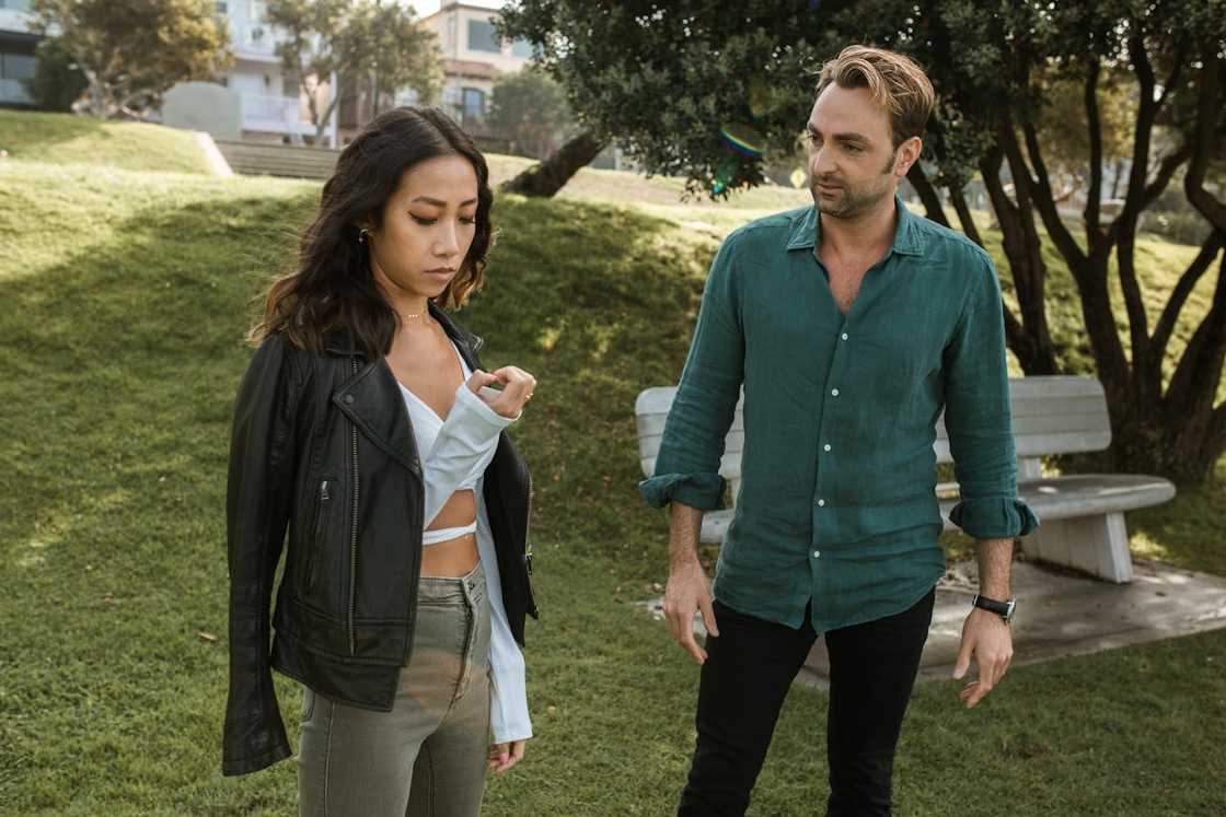 Two people stand in a park-like setting with green grass and trees.