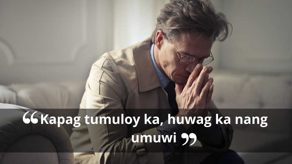 A man sits leaning forward with his hands clasped near his face, appearing deep in thought.