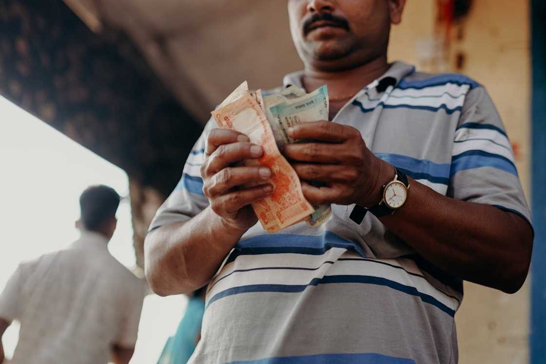 A person holding and counting worn paper money outdoors.