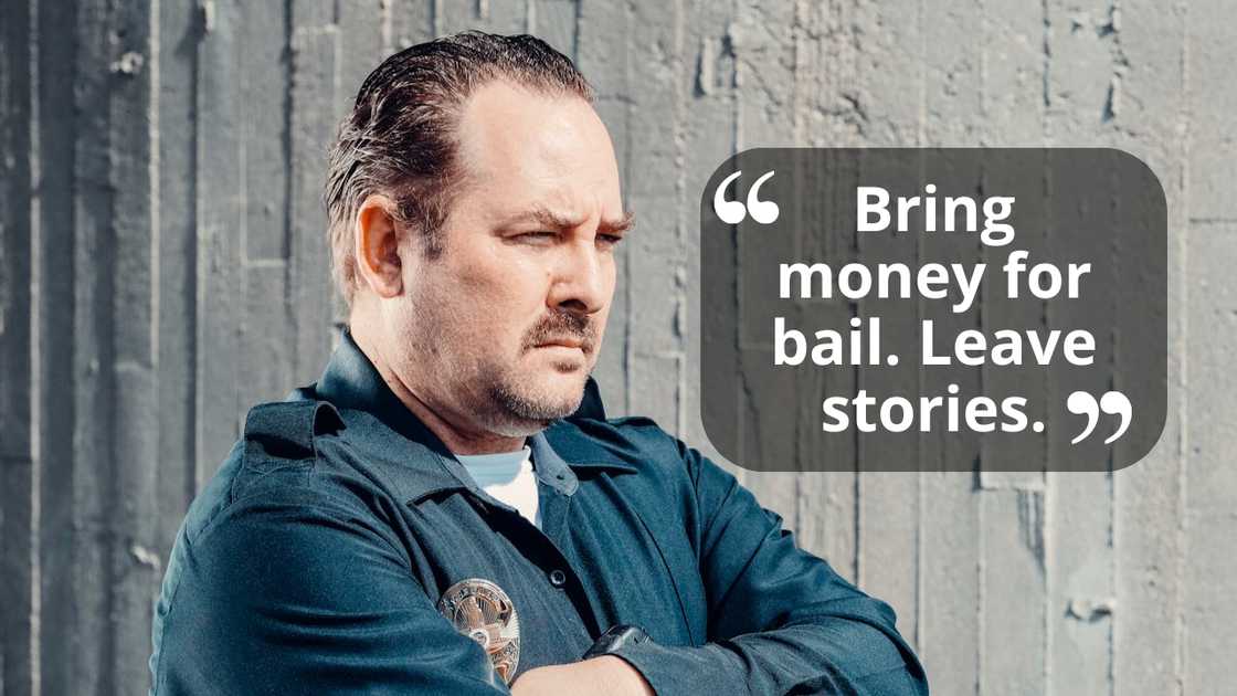 A man in a uniform stands with his arms crossed, looking serious against a concrete wall.