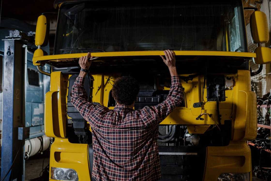 A mechanic repairs the front of a truck using tools.