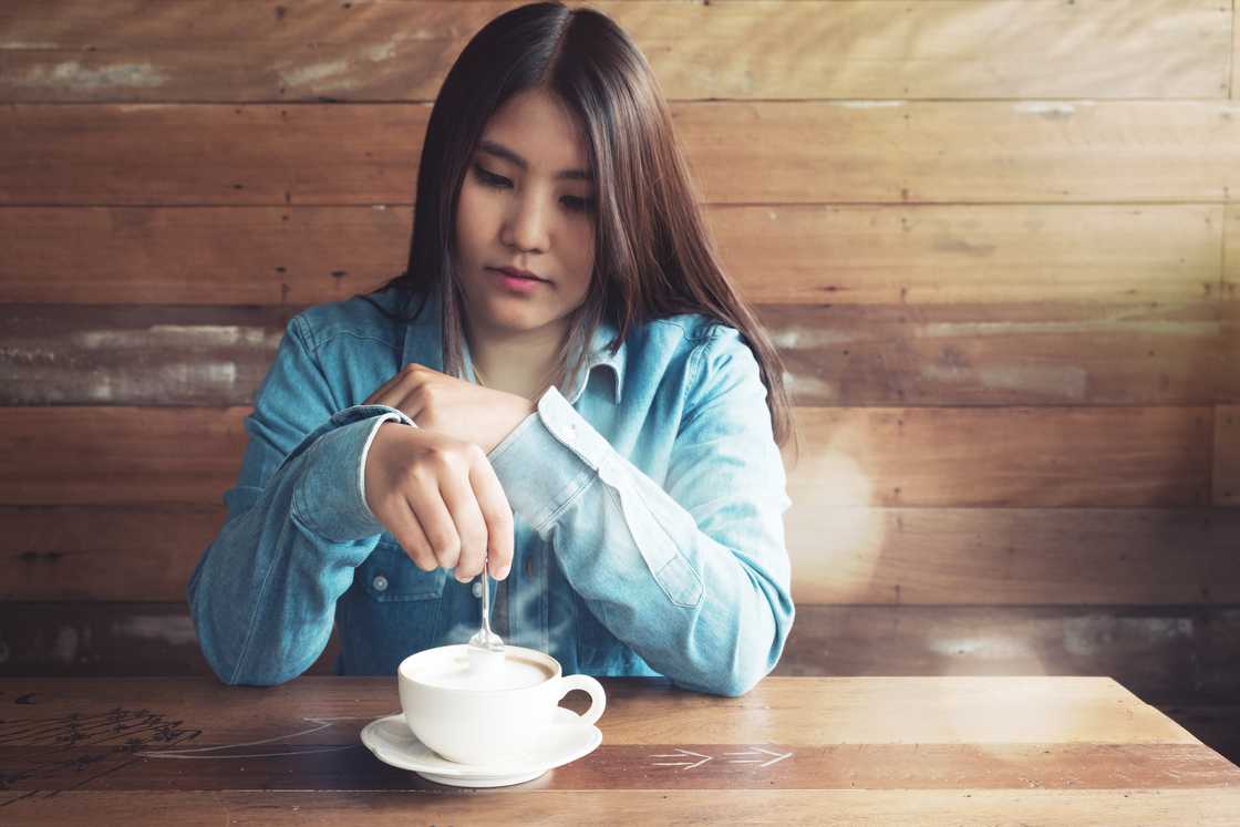 A young woman stirring her coffee at coffee shop. A young woman stirring her coffee at coffee shop.