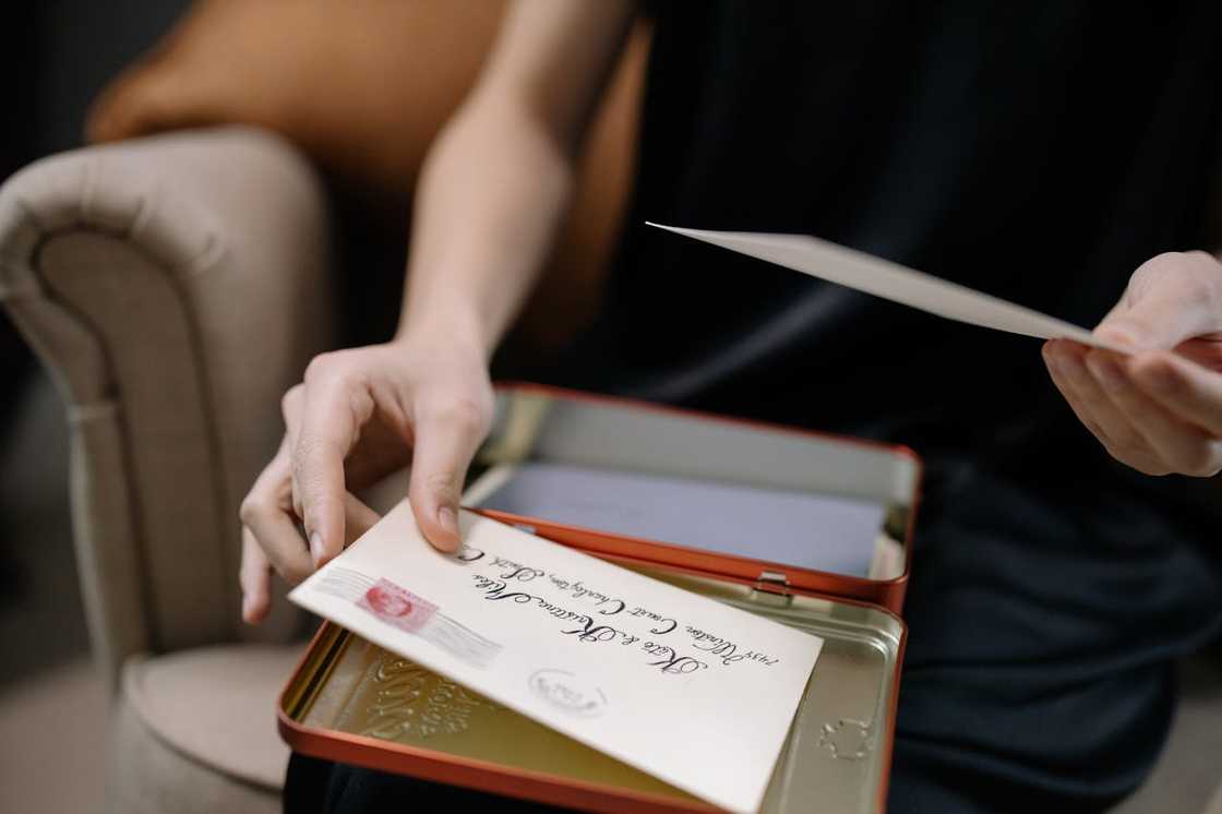 Close-up of a person opening a metal box and holding an old envelope with handwritten text. Close-up of a person opening a metal box and holding an old envelope with handwritten text.