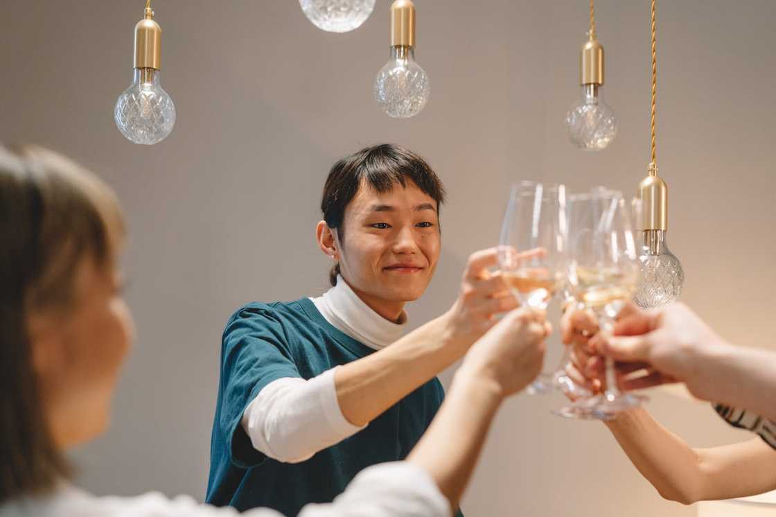 Friends clinking wine glasses in a toast under hanging pendant lights.