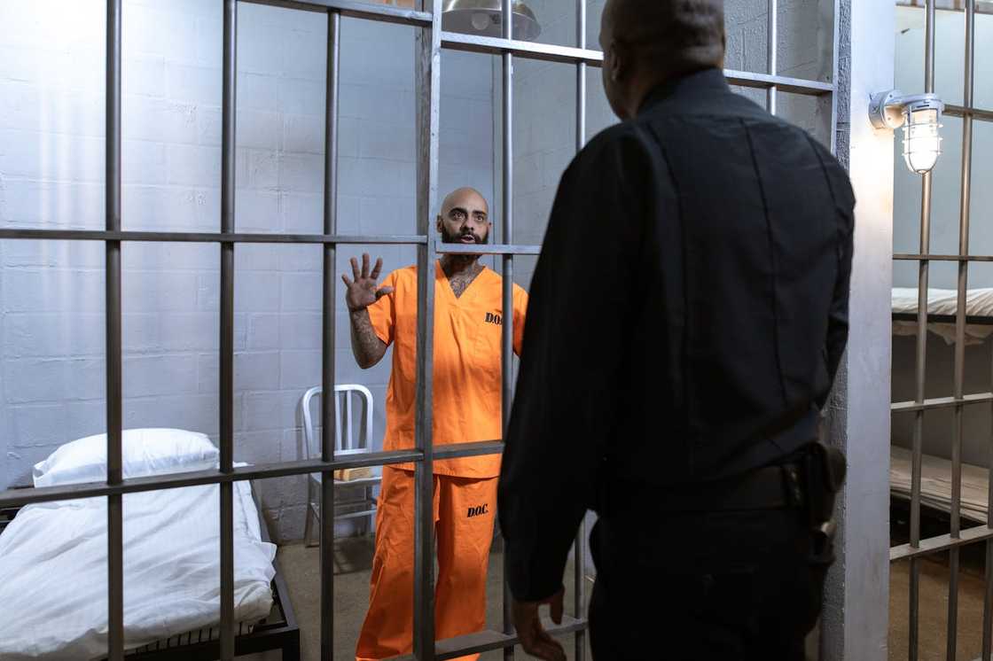 An inmate in an orange uniform speaks to a guard through jail bars. An inmate in an orange uniform speaks to a guard through jail bars.