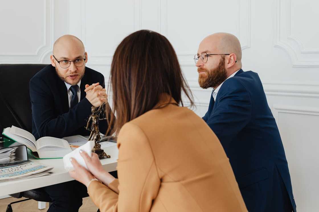 Two men speak with a woman at a desk.