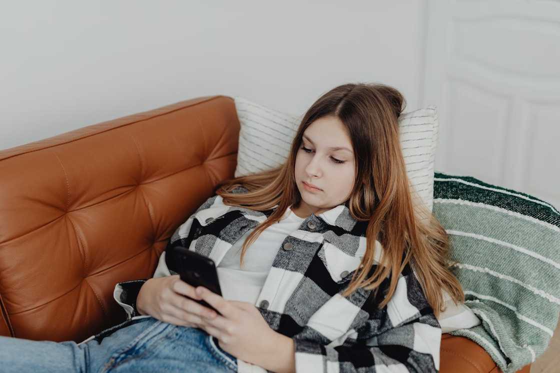A teenage girl lies on a couch scrolling on her phone. A teenage girl lies on a couch scrolling on her phone.