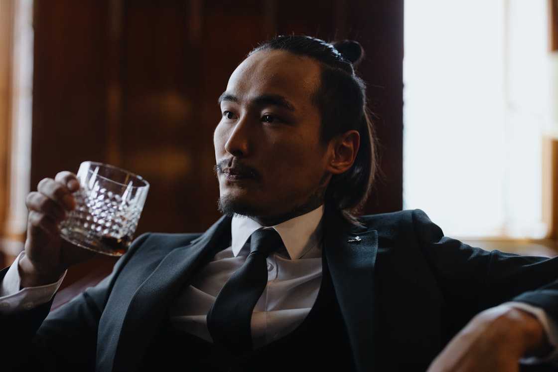 A man in a black suit drinks from a glass.
