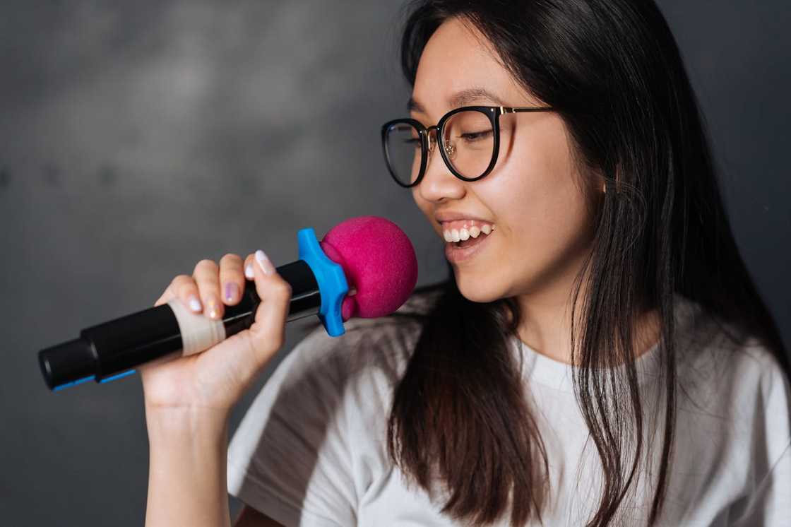 A woman smiles while singing into a microphone. A woman smiles while singing into a microphone.