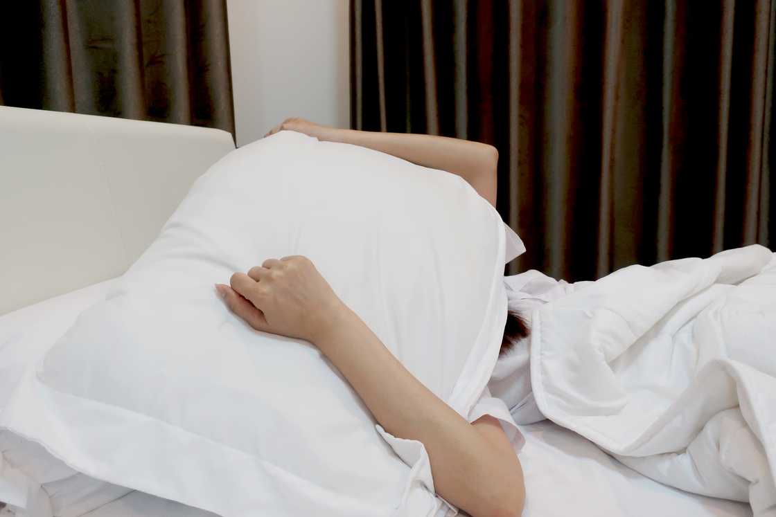 A woman covering her head with pillow on the bed