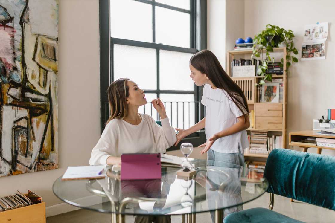 Two people talk indoors near large windows. Two people talk indoors near large windows.