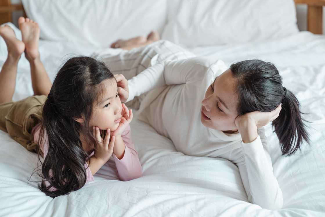 A mother and her daughter talking while lying on the bed.