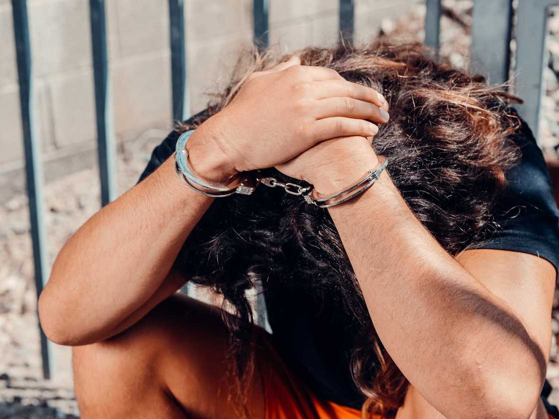 A distressed person sits outdoors with handcuffs on.
