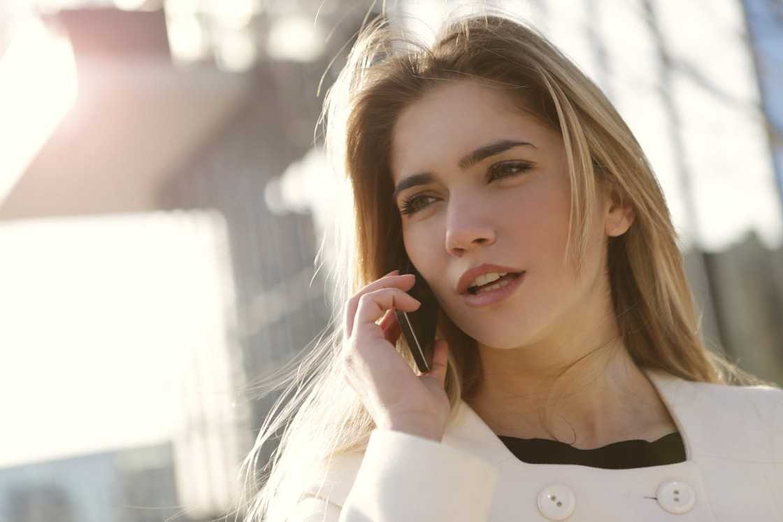 A woman talking on a mobile phone outdoors in sunlight.