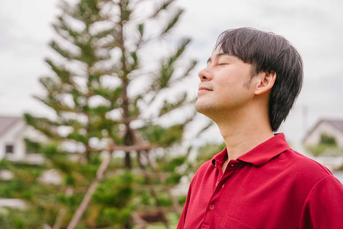 A cheerful man standing outside with his eyes closed enjoying a moment of peace.