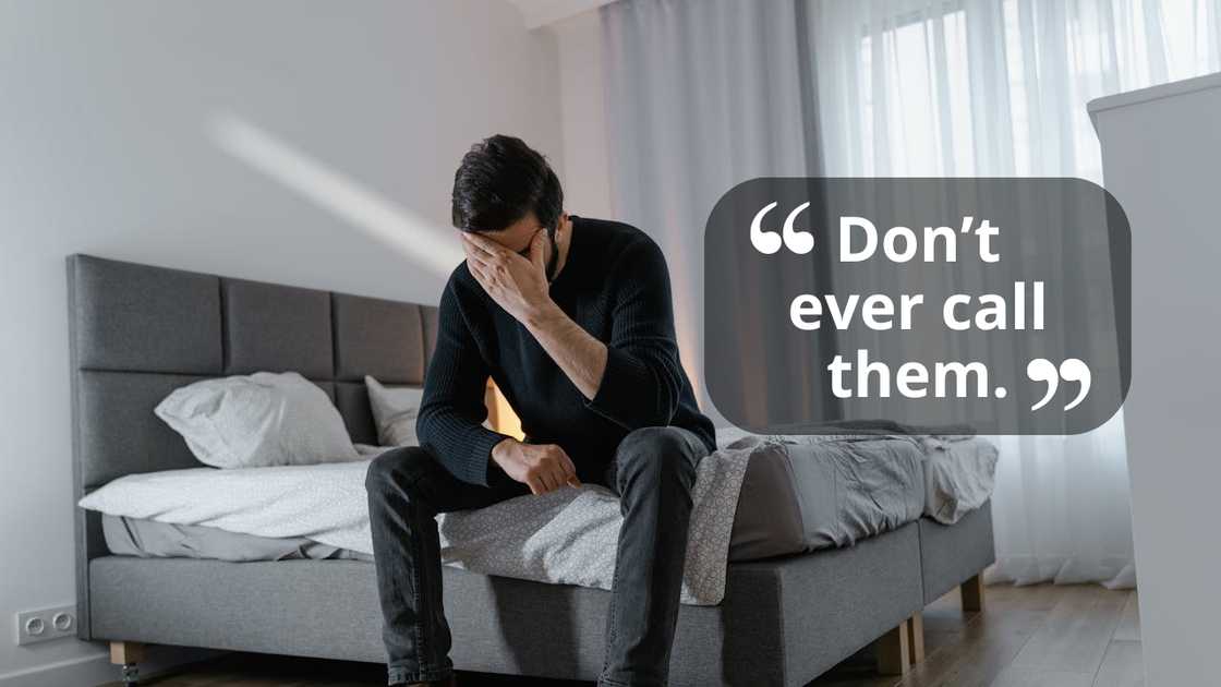 A man sits on the edge of a bed in a bedroom, covering his face with one hand in distress.