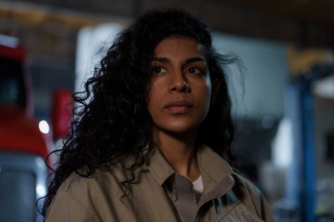 A woman looking ahead thoughtfully in a dim workshop.