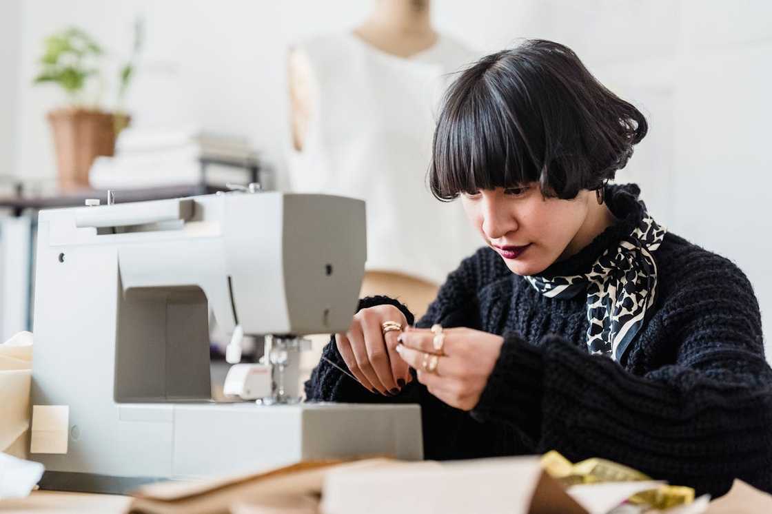 A woman adjusting the thread while working at a sewing machine.
