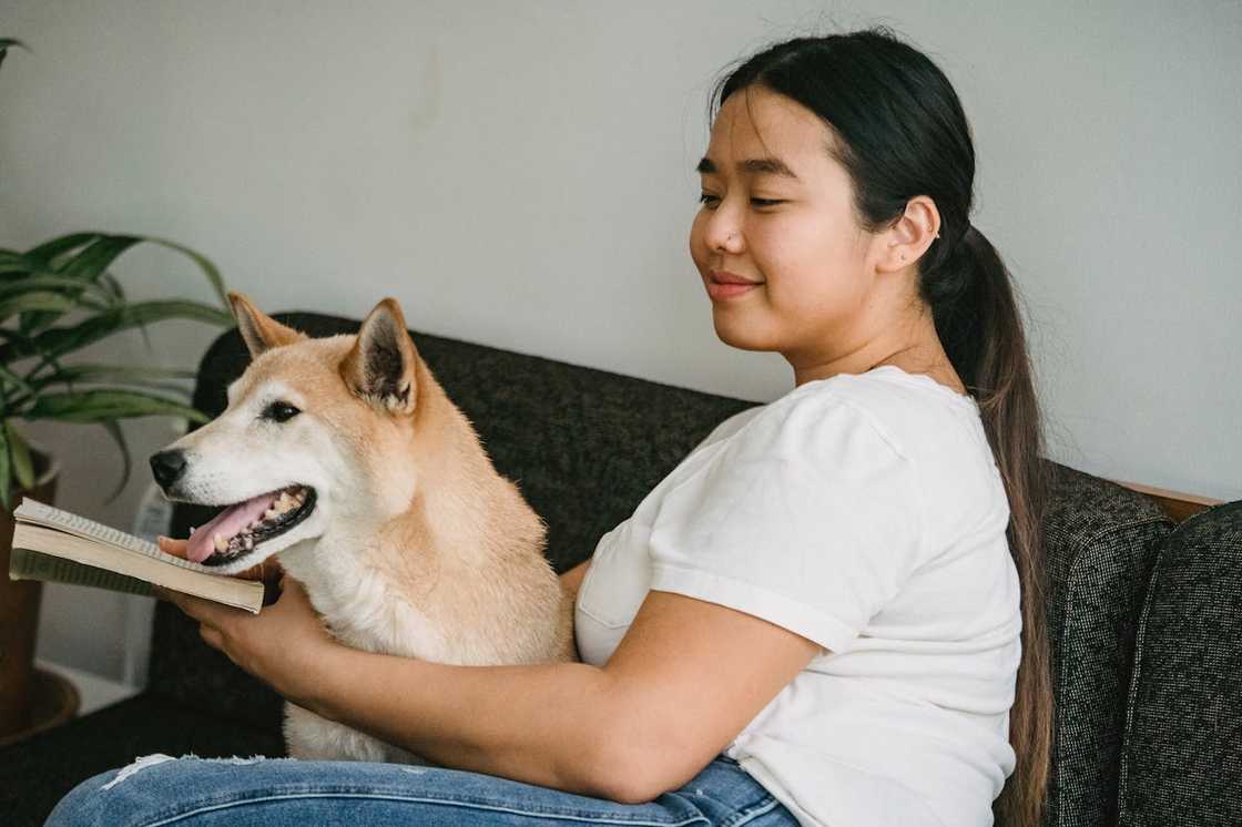 A young woman reads a novel while petting her dog.