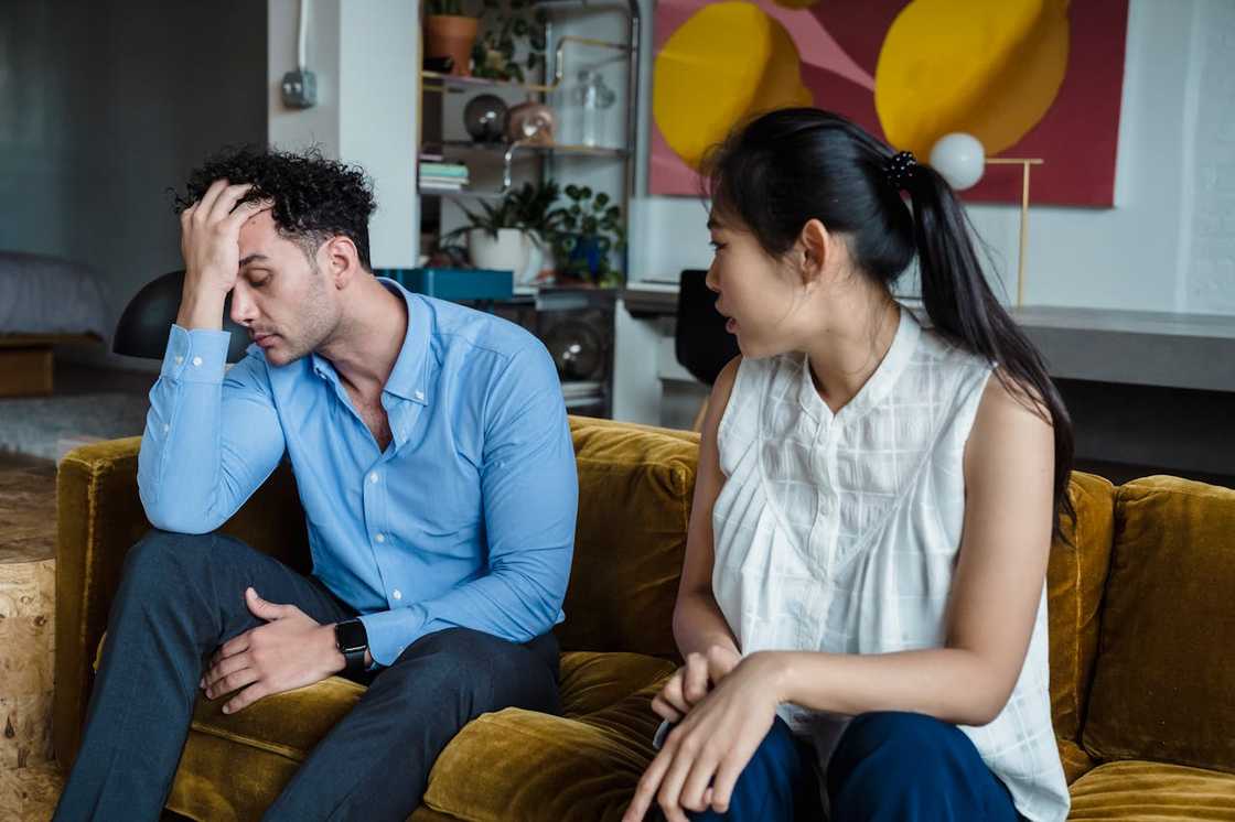 A couple argues in a living room while seated on a sofa. A couple argues in a living room while seated on a sofa.
