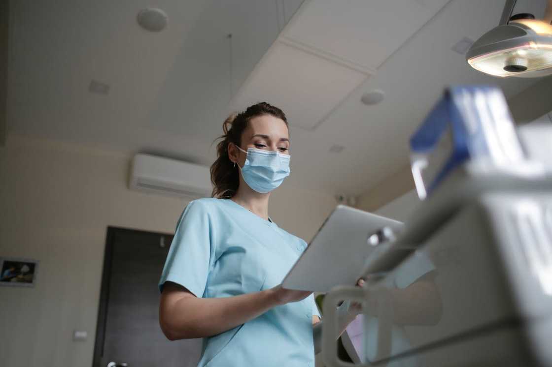 A nurse stands besides a patient's bed holding a file. A nurse stands besides a patient's bed holding a file.