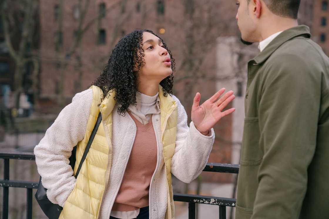 A woman raises her hand as she speaks to a man outdoors. A woman raises her hand as she speaks to a man outdoors.