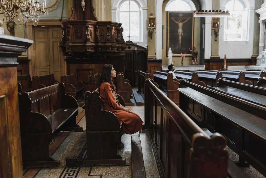 A woman sits alone in a church pew, facing forward in quiet reflection.