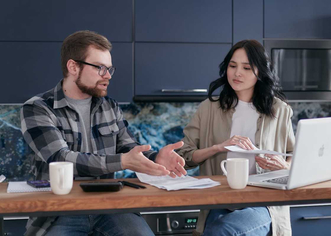 Two adults sit in a home setting, reviewing a piece of paper together. Two adults sit in a home setting, reviewing a piece of paper together.
