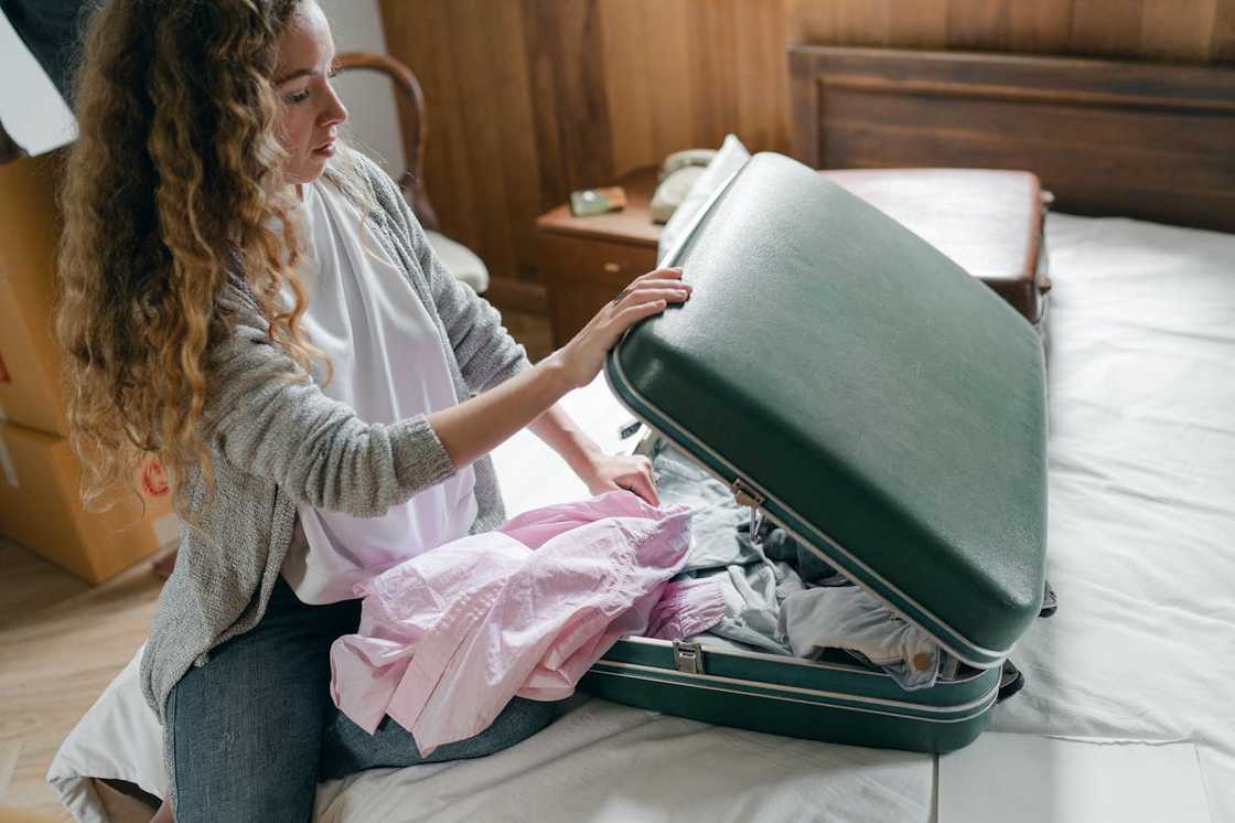 A woman packs her clothes into a suitcase on a bed, preparing to leave.