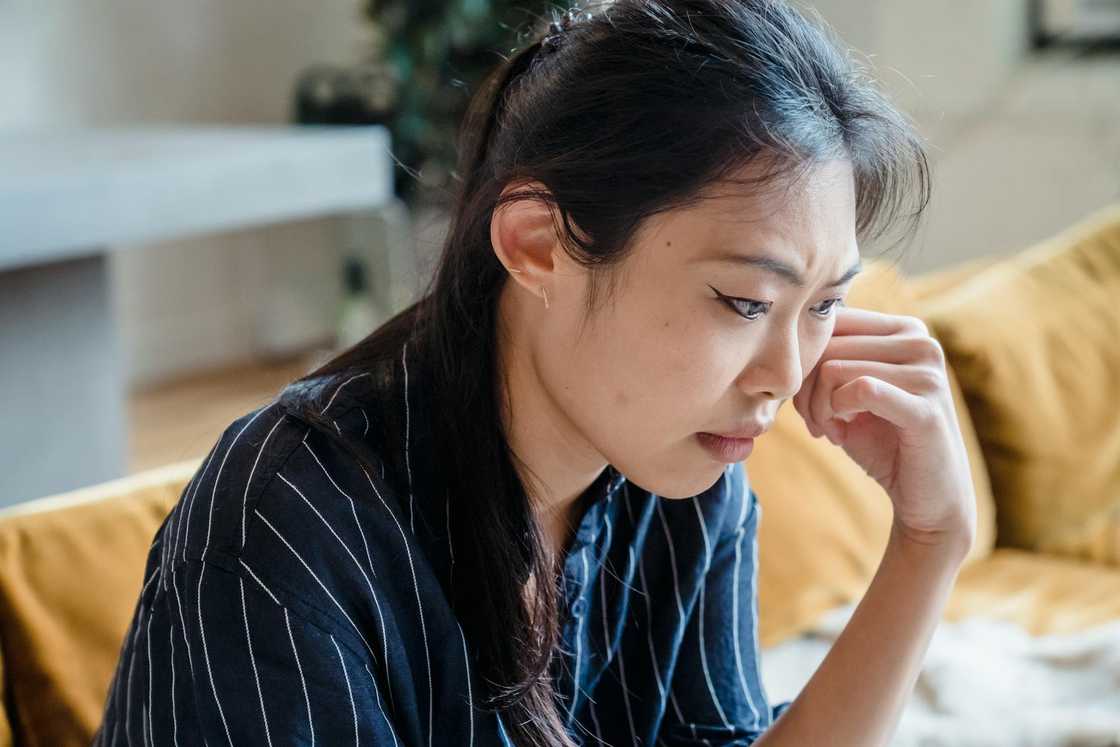 A woman sitting on a couch looks worried and deep in thought.