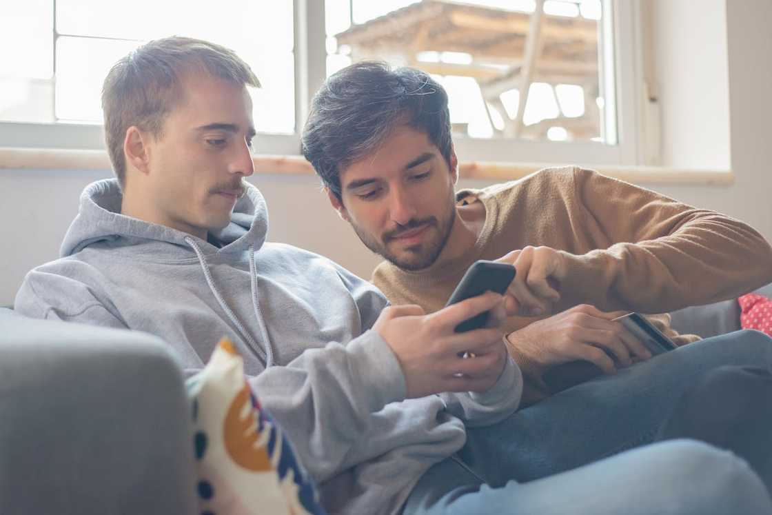 Two people sit on a sofa, looking at a smartphone together.