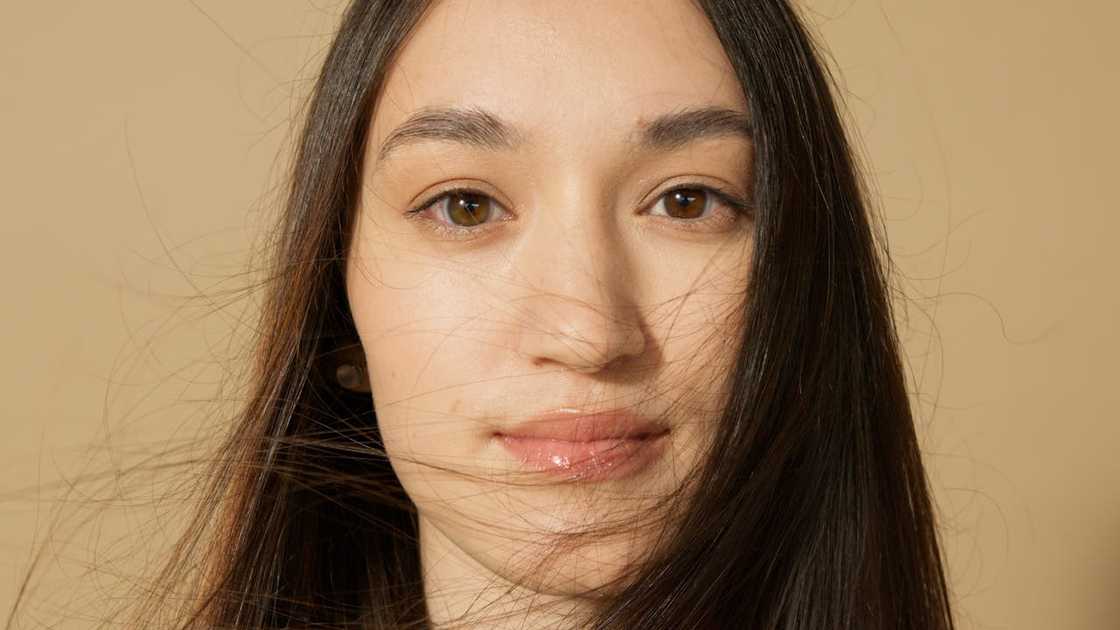 A close-up portrait of a woman with long dark hair and a neutral expression against a plain background.
